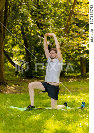 Athletic sporty fit man doing workout yoga breathing exercise on sports mat raising hands in park Athletic sporty fit man doing workout yoga breathing exercise on sports mat raising hands in park 117518742