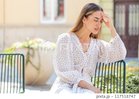 Woman rubbing temple to cure headache problem suffering from tension migraine stress on city street 117518747