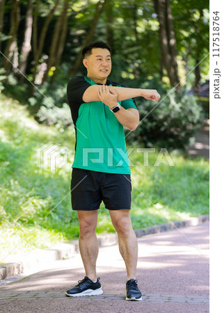 Japanese sporty healthy man athlete in park outdoors stretching hands stretch arms morning workout Japanese sporty healthy man athlete in park outdoors stretching hands stretch arms morning workout 117518764