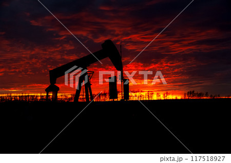 Striking orange and purple sunrise in prairies and the silhouette of an oil pump extracting fuel. 117518927