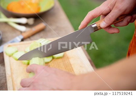 Close up of man holding sharp knife, chopping cucumber. Preparing vegetables for an outdoor barbecue. Close up of man holding sharp knife, chopping cucumber. Preparing vegetables for an outdoor barbecue. 117519241
