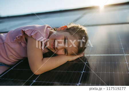 Cute girl lying on solar panels roof, shot with copy space. Rooftop solar or photovoltaic system. Sustainable future for next generation. 117519277