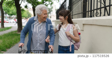 Grandma picking up girl after first day of school. Granddaughter spending time with senior grandmother outdoors in city. Grandma picking up girl after first day of school. Granddaughter spending time with senior grandmother outdoors in city. 117519326