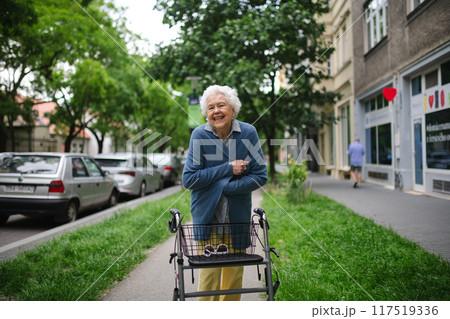Beautiful elderly woman walking on city street with rollator, going shopping to the store. Feeling cold. Beautiful elderly woman walking on city street with rollator, going shopping to the store. Feeling cold. 117519336