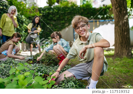 Students and female teacher at outdoor sustainable education class. Kids taking care of plants in school garden. Concept of experiential learning and ecoliteracy. Students and female teacher at outdoor sustainable education class. Kids taking care of plants in school garden. Concept of experiential learning and ecoliteracy. 117519352