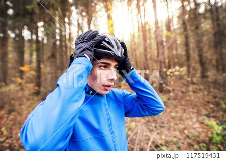 Man putting on helmet before ride on bike in the middle of forest, early autumn morning. Concept of healthy lifestyle. Man putting on helmet before ride on bike in the middle of forest, early autumn morning. Concept of healthy lifestyle. 117519431