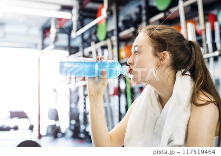 Young fitness girl with dental braces feeling exhausted after hard workout in gym, drinking water. Young fitness girl with dental braces feeling exhausted after hard workout in gym, drinking water. 117519464
