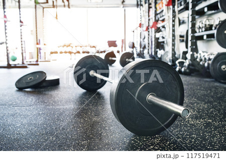 Rows of metal barbells on floor and rack for strength training in gym. 117519471