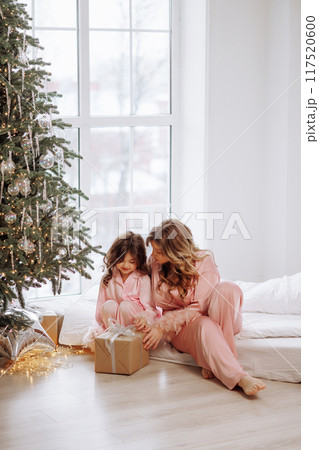 A woman and a child are sitting on a bed in front of a Christmas tree 117520600