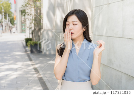 オフィス街で眠くてあくびをしているビジネスウーマン 117521036