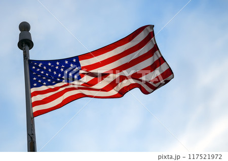 American Flag Waving Against a Cloudy Sky with Sunlight 117521972