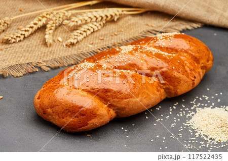 Freshly baked braided bread with sesame seeds on rustic background, ideal for bakery food projects 117522435
