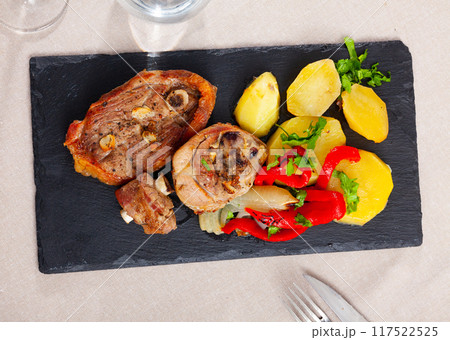 Fried lamb leg steaks with potatoes, red pepper slices, greens on slate board Fried lamb leg steaks with potatoes, red pepper slices, greens on slate board 117522525