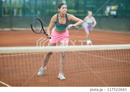 Focused girl playing doubles tennis on outdoor court Focused girl playing doubles tennis on outdoor court 117522683