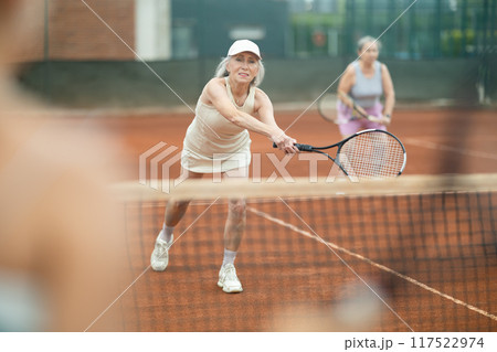 Two elderly women playing doubles tennis 117522974