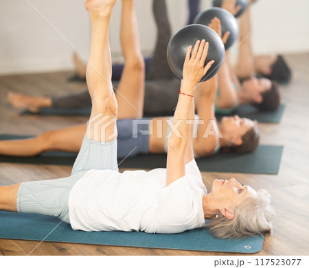 Elderly woman doing pilates with soft ball in group 117523077