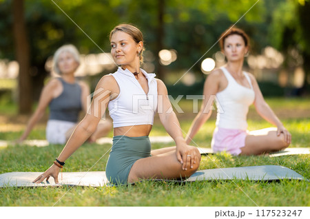 Female yoga instructor stretching in Padmasana pose with group in park 117523247