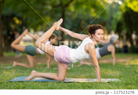 Positive sporty skilled young female teacher demonstrating table pose of yoga in green park at daytime Positive sporty skilled young female teacher demonstrating table pose of yoga in green park at daytime 117523276