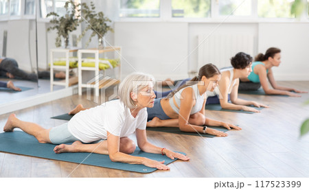 Group of women practicing pigeon pose of yoga on mat in fitness room 117523399