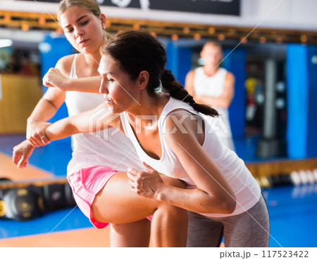 Young girl practicing elbow and knee strikes while locked arm with female opponent 117523422