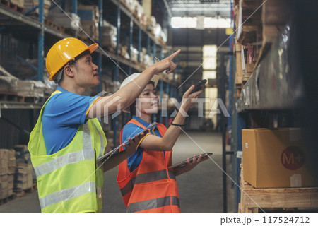 Warehouse management team check stock inventory. Asian men women worker use bar code scaner scan goods shelf writing checklist on clipboard. Teamwork logistics staff counting products store inventory 117524712