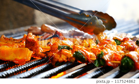 BBQ Barbecue grilled meat stick on fire flame with hot charcoal cooking outside. Beef grilling picnic outdoor with smoke bacon spicy sausage for party. Grill pork bbq on fire flame BBQ Barbecue grilled meat stick on fire flame with hot charcoal cooking outside. Beef grilling picnic outdoor with smoke bacon spicy sausage for party. Grill pork bbq on fire flame 117524862