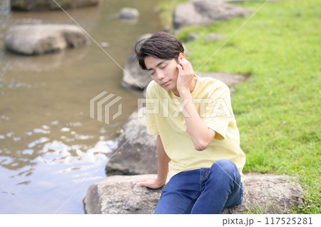 夏の水辺で涼んで音楽を聴く若い男性 117525281