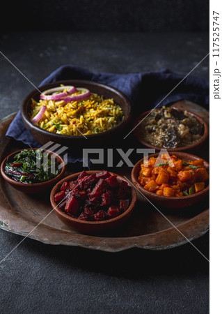 An assortment of vibrant, flavorful vegetarian Pakistani and Indian dishes, including biryani rice, served in bowls on a rustic platter An assortment of vibrant, flavorful vegetarian Pakistani and Indian dishes, including biryani rice, served in bowls on a rustic platter 117525747