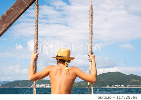 Teen boy on swing with scenic sea view and mountains in the background. 117528368