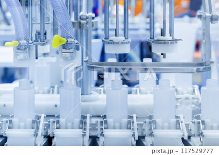 robot arm moving plastic bottle to conveyor belt of auto capping and labeling machine at cosmetic and skin care manufacturing. cosmetic industry and ai technology machinery concept. 117529777