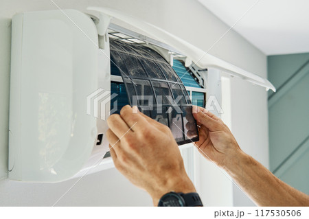 Air conditioner maintenance. Male technician repairs home climate system in living room. Man is cleaning filters of conditioner Air conditioner maintenance. Male technician repairs home climate system in living room. Man is cleaning filters of conditioner 117530506