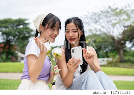 Two lovely women are enjoying a conversation while looking at something on a phone during a picnic. 117531186