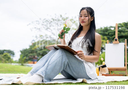 A beautiful Asian woman sitting on a picnic blanket in a park, posing and smiling at the camera. A beautiful Asian woman sitting on a picnic blanket in a park, posing and smiling at the camera. 117531198