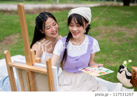 Two positive and lovely young Asian women are enjoying painting on a canvas easel together in a park Two positive and lovely young Asian women are enjoying painting on a canvas easel together in a park 117531207
