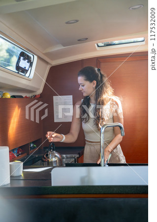 Young woman standing and preparing tea in kitchen in cabin of modern yacht during sailing in sea. Yacht life concept Young woman standing and preparing tea in kitchen in cabin of modern yacht during sailing in sea. Yacht life concept 117532009
