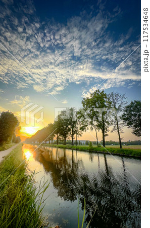 A Serene Sunset Over a Tranquil River, Surrounded by Lush Green Trees and Rolling Hills A Serene Sunset Over a Tranquil River, Surrounded by Lush Green Trees and Rolling Hills 117534648
