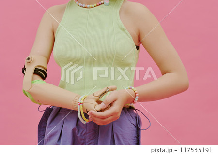 Midsection of unrecognizable teen girl with arm prosthesis wearing stylish clothes posing for camera in studio, pink background Midsection of unrecognizable teen girl with arm prosthesis wearing stylish clothes posing for camera in studio, pink background 117535191