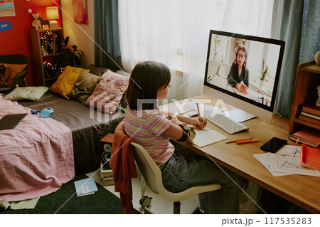 Modern teen girl with prosthetic arm sitting at desk and looking at screen while having online lesson with school teacher Modern teen girl with prosthetic arm sitting at desk and looking at screen while having online lesson with school teacher 117535283