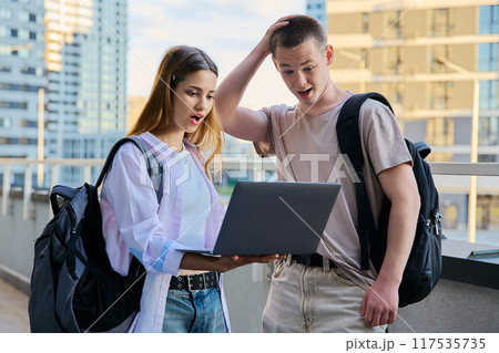 Surprised teenage college age students looking at laptop screen, modern city background Surprised teenage college age students looking at laptop screen, modern city background 117535735