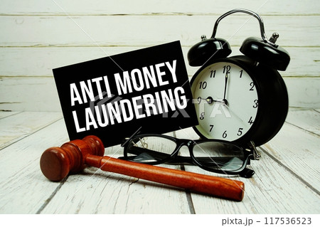 Anti Money Laundering text on paper card with alarm clock and wooden judge gavel on wooden background 117536523