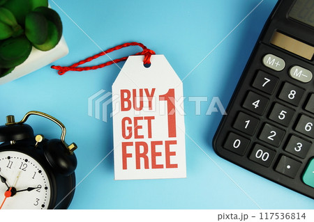 Top view of Buy One Get One Free text on tag sale with calculator and black alarm clock flat lay on blue background 117536814