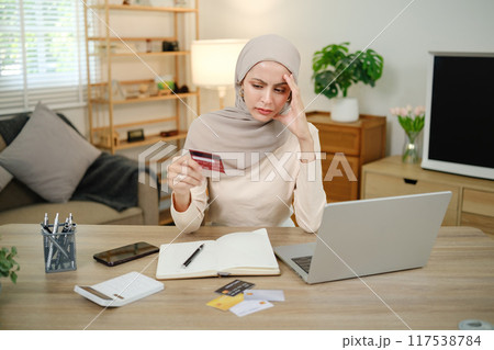 A woman is sitting at a desk with a laptop and a stack of credit cards 117538784