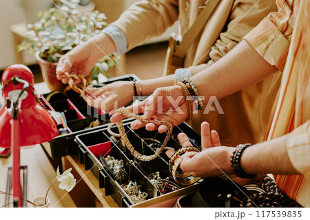 Close-up of hands choosing necklace and bracelets from display in jewelry shop showing intricate details and accessories being examined and selected with care 117539835