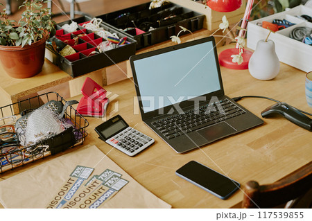 Home office desk featuring laptop, smartphone, and calculator alongside office supplies, plants, and decorations creating an organized and functional workspace 117539855