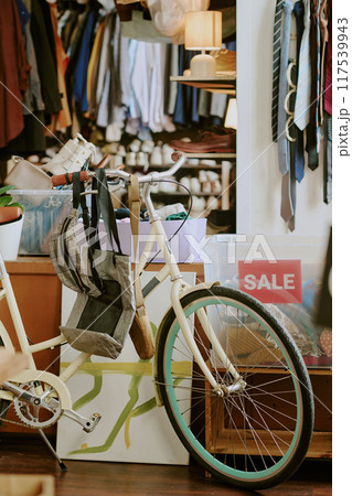 Bicycles, a backpack, and shelves full of clothing and accessories seen in cozy thrift store interior with an organized, eclectic mix of items and sale signage visible Bicycles, a backpack, and shelves full of clothing and accessories seen in cozy thrift store interior with an organized, eclectic mix of items and sale signage visible 117539943