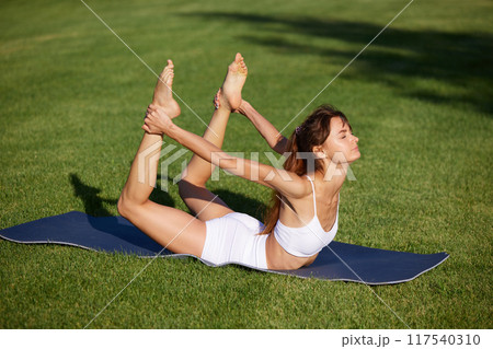 Calm and quiet morning. Flexible, beautiful young woman doing yoga exercises for spine at park bathed in sunbeams. Calm and quiet morning. Flexible, beautiful young woman doing yoga exercises for spine at park bathed in sunbeams. 117540310
