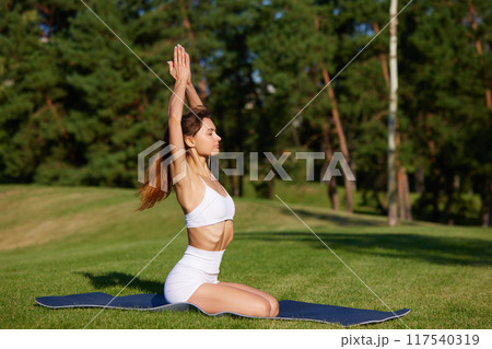 Morning practice for to fill with energy. Woman doing yoga exercises in early, sunny morning at park. 117540319
