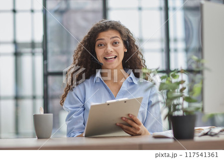 Brunette business woman using headset to communicate and advise people in customer service office. 117541361