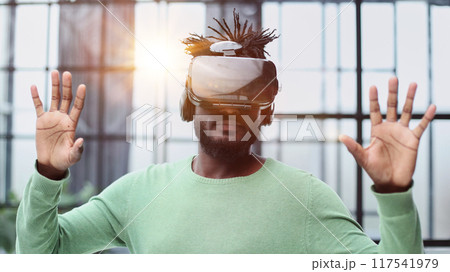 Cool handsome african american man put on virtual reality goggles for the first time in the office. 117541979