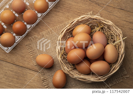 Heap of Chicken eggs on wicker basket on wooden plate background.Top view 117542007